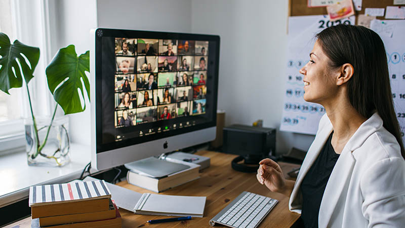 Joven mirando una pantalla de computadora, en donde hay una videoconferencia