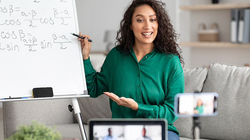 Mujer mostrando fórmulas matemáticas en una pizarra, mientras está conectada en una videoconferencia