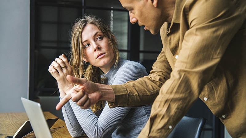 A young man explaining something to a young woman who is working on a computer