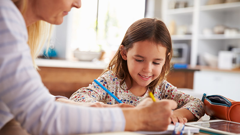 A teacher working with a girl at a desk, with pencils and a tablet