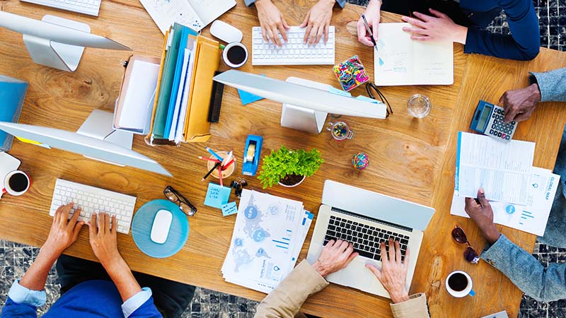 A table with papers, tech devices, and hands working together