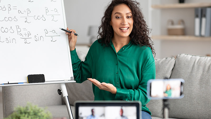 A woman writing mathematical formulas on a whiteboard while participating in a video conference