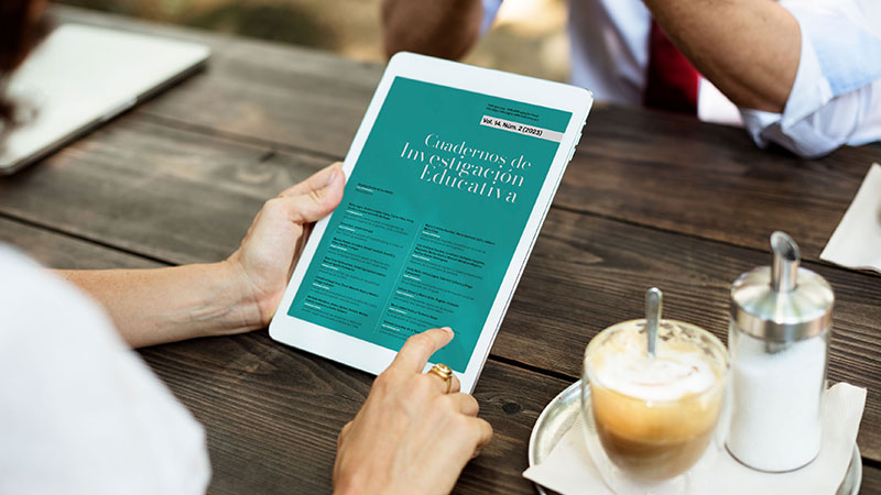 A hand clicking on a tablet, displaying the cover of the magazine *Cuadernos de Investigación Educativa*