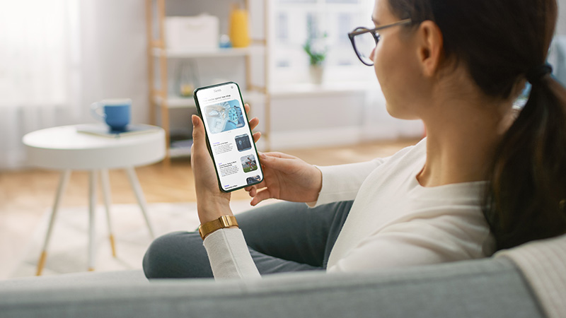 A woman on the couch, holding a cell phone, scrolling through social media