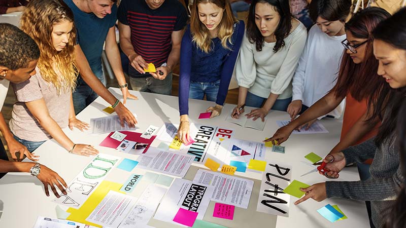 Grupo de jovenes, trabajando en equipo, con papeles de colores sobre una mesa